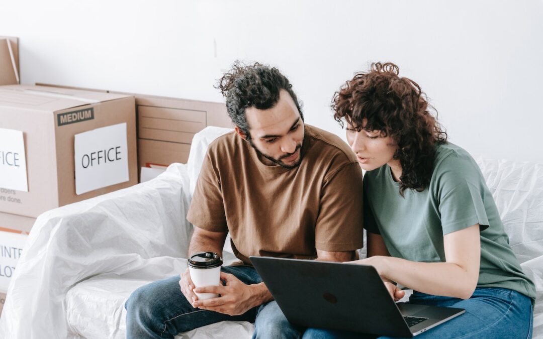 : A man and woman sitting on a couch beside moving boxes.