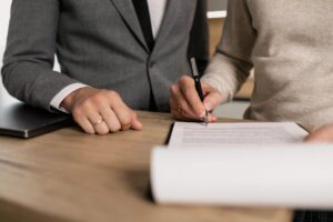 A person signing a contract with the other person standing right next to them