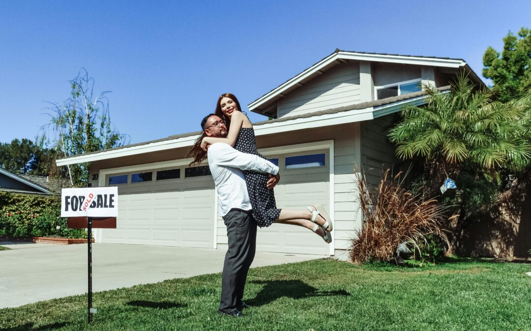 Couple in front of their new home, man holding the woman up