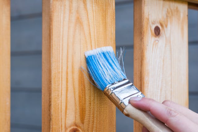 Person painting a wooden fence